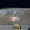 Ночь на пляже. На парапете установлен лоток для приема монет. На дальнем плане зажжены свечи. Ночной прибой ласкает прибрежный песок. Атмосфера романтики и покоя. Песок мелкий и желтый.